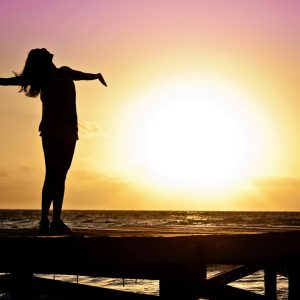 A joyful silhouette of a woman standing on a dock at sunset, embracing the freedom of nature.