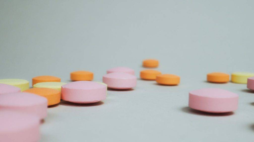A close-up of pink, orange, and yellow tablets on a plain white surface. Ideal for health and pharmaceutical themes.